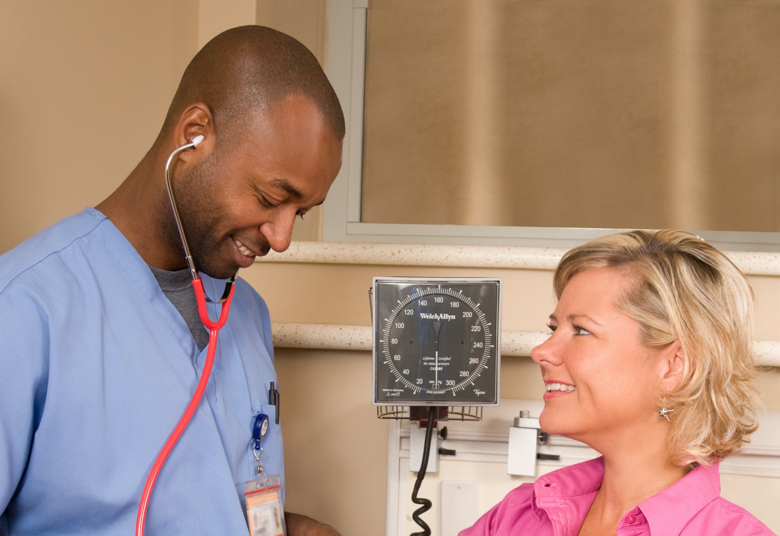 A clinician in blue scrubs checking a patient's blood pressure at home